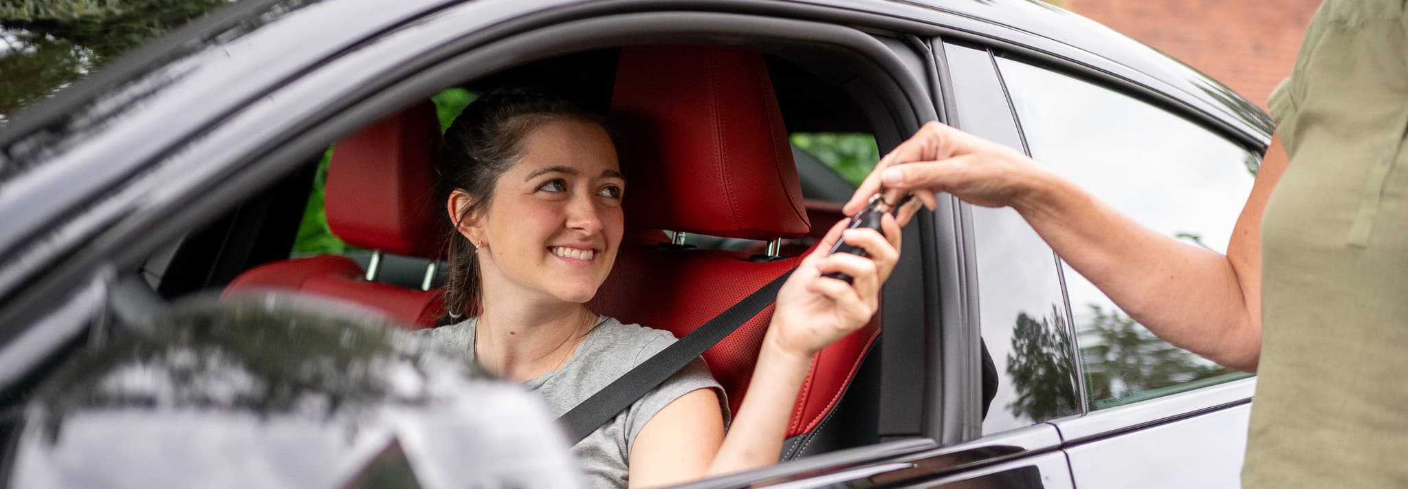 Teenage girl recieving car keys from parent through car door window