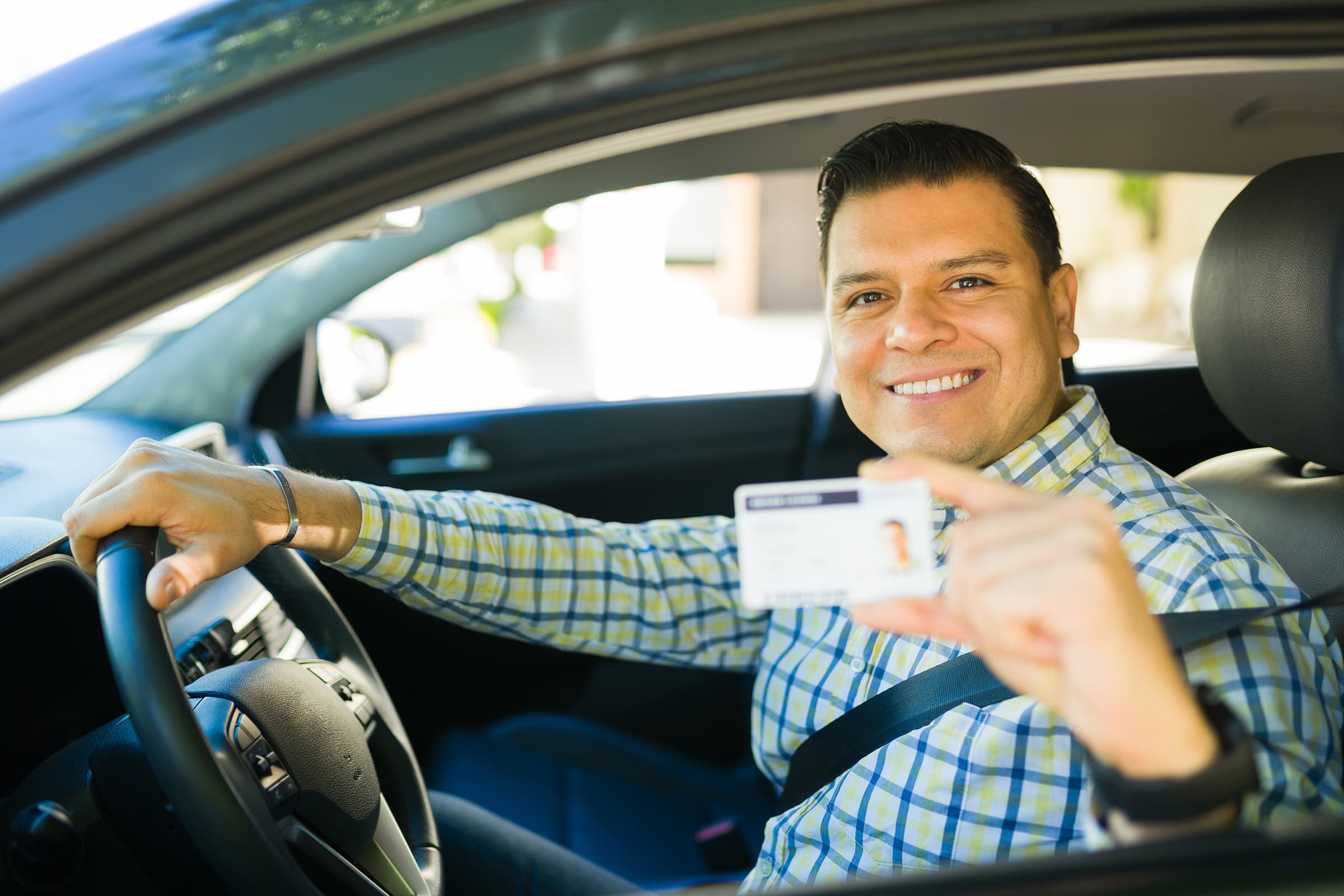 Man smiling in car, showing driver's license