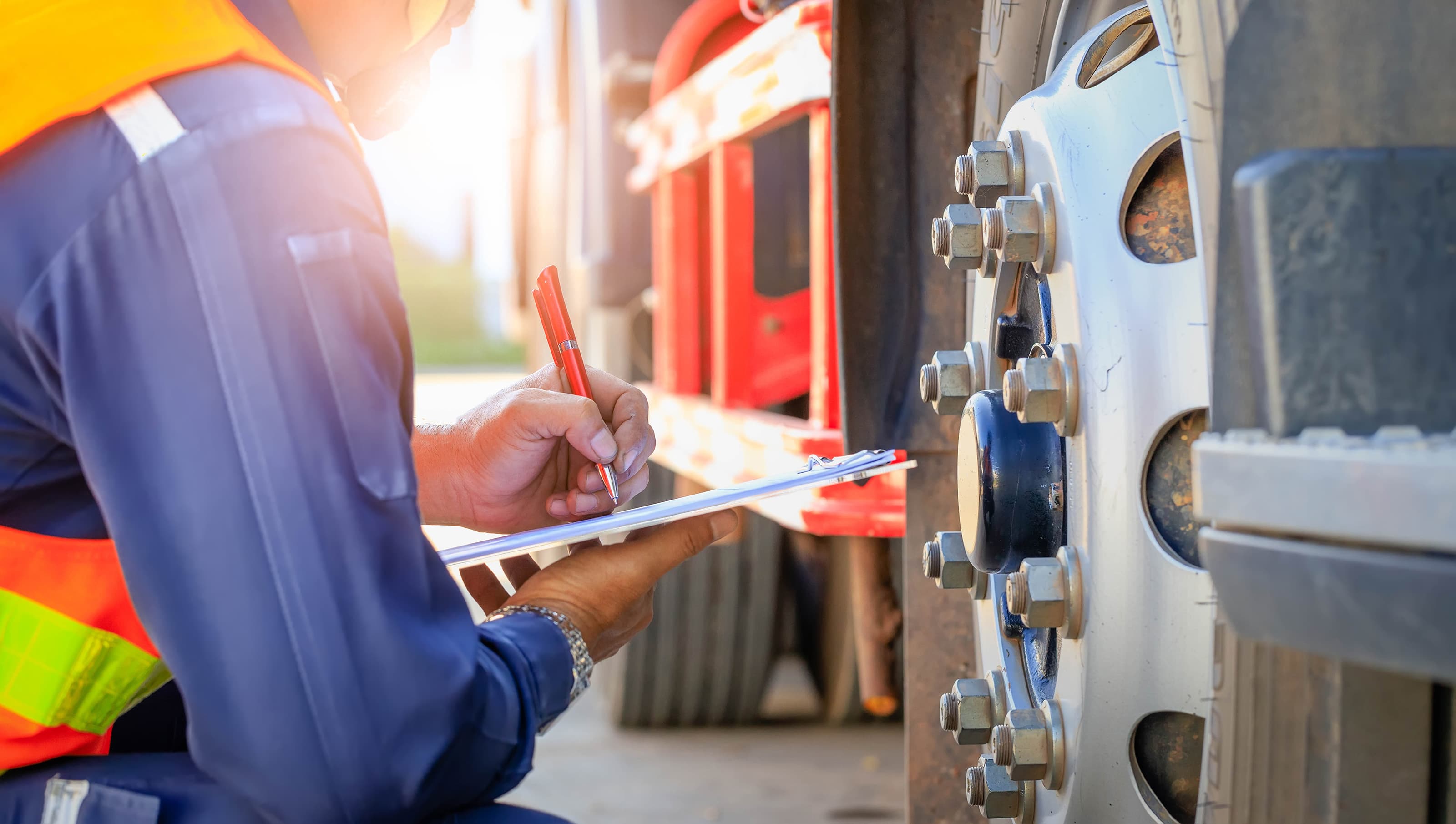 Worker kneeling with clipboard as they check the state of a truck